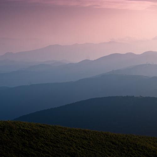 Mehrere Bergketten im Dunst unter rosafarbenem Himmel.